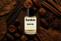 Scentivia Dark Fuel perfume bottle surrounded by dried figs, dates, cinnamon sticks, star anise pods, vanilla beans, and dried brown leaves on a dark brown textured surface.