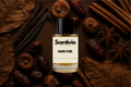 Scentivia Dark Fuel perfume bottle surrounded by dried figs, dates, cinnamon sticks, star anise, vanilla pods, and textured brown leaves on a dark mahogany background.