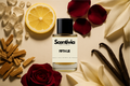 Scentivia Fifth Lie perfume bottle arranged flat on a light beige surface surrounded by a lemon slice, red rose petals, a whole red rose, white lily petals, whole vanilla beans, a pile of wood chips, and small translucent resin pieces.