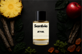 Scentivia Jet Fuel perfume bottle arranged flat on a black surface surrounded by a pineapple round, a whole red apple, pieces of tree bark, dark green leaves, clumps of green moss, and translucent amber resin chunks.