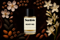 Scentivia Velvety Vice perfume bottle arranged flat on a dark brown fabric background, bordered by coffee beans, almonds, dark tonka beans, pink blossoms, and white tubular flowers.