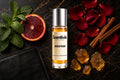 Gold Flex roll on bottle with mint leaves, blood orange slice, rose petals, cinnamon sticks and amber crystals on marble background
