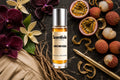 Orchid Kiss roll on bottle with Orchid flowers, Vanilla pods, Passionfruit, Lychee and Vetiver roots on dark marble background